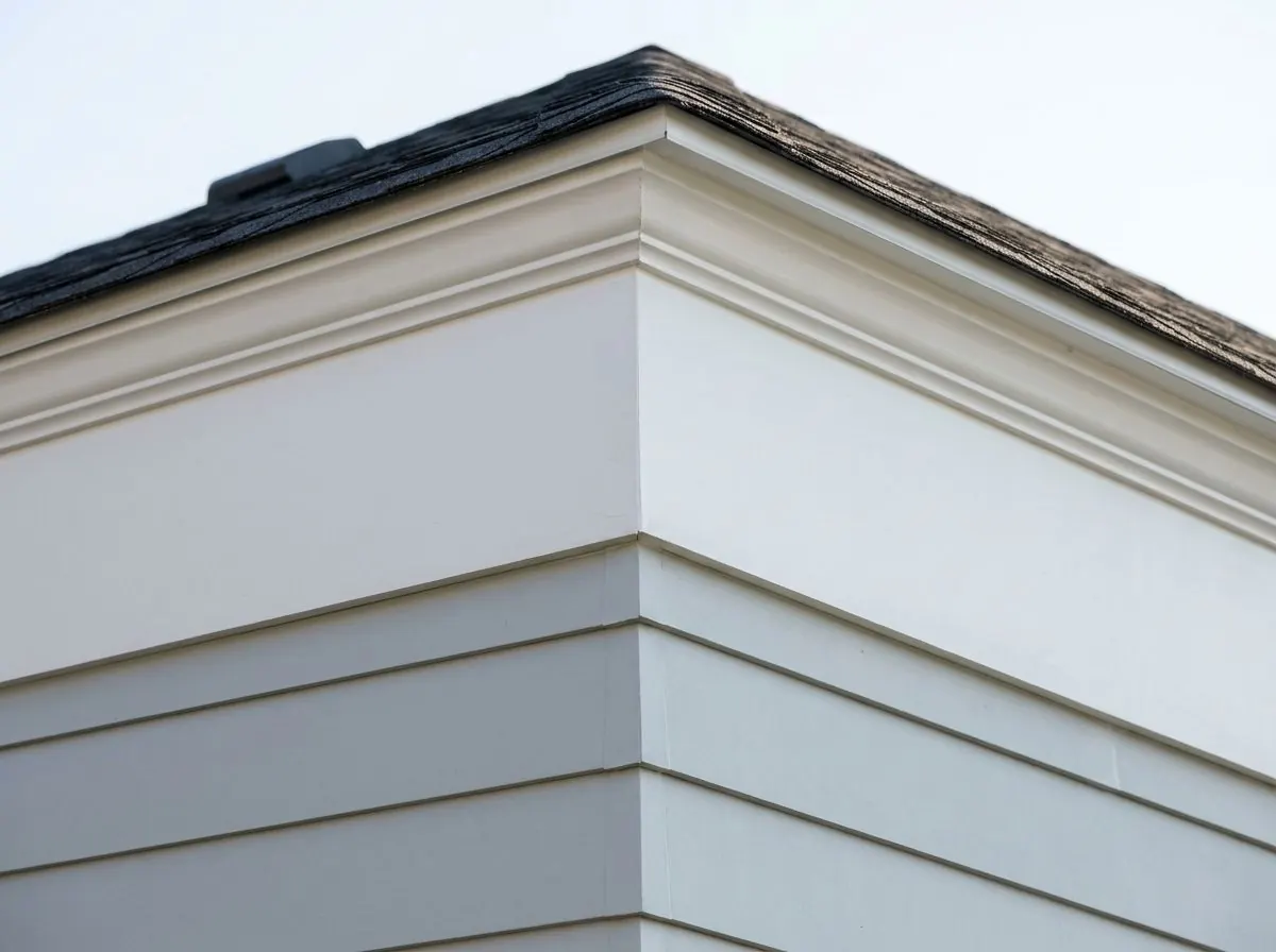 A white frieze board and crown moulding run beneath the eave of a house above pale grey lap siding.